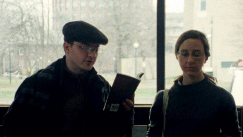 Classical Period film still. Man reading book next to woman in glasses. Ted Fendt movie.