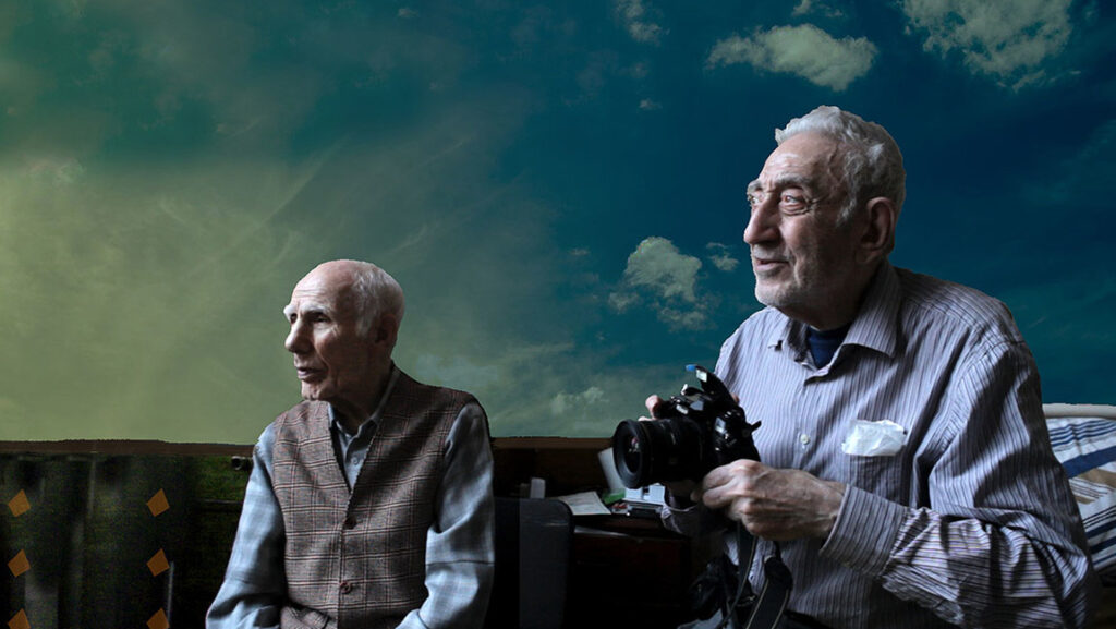 Distant Constellation | Shevaun Mizrahi Shevaun Mizrahi's Distant Constellation: Two elderly men, one holding a camera, against a sky backdrop.