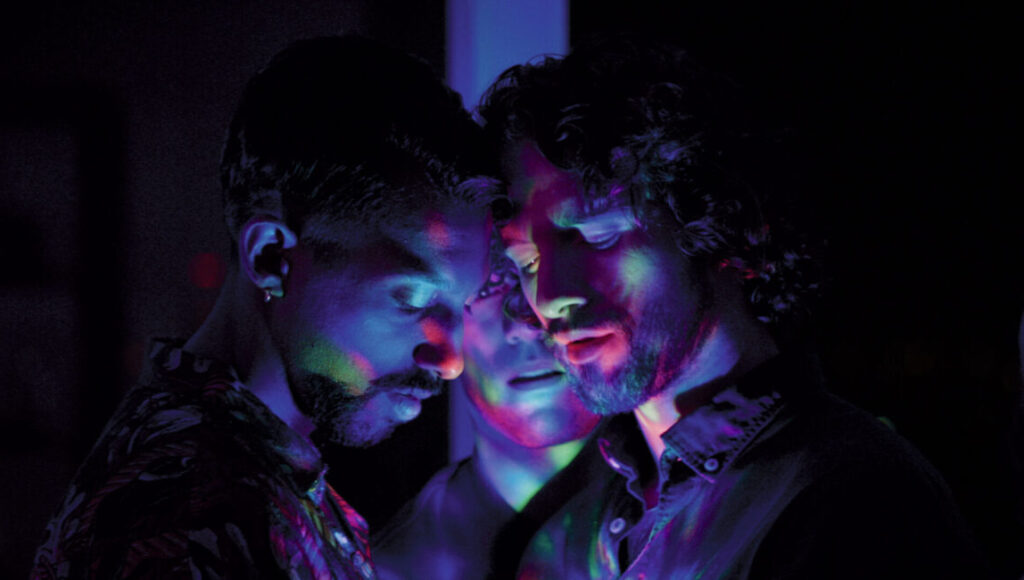 Don't Look Down film still. Three men, Olivier Ducastel & Jacques Martineau movie, bathed in colorful, vibrant neon light.