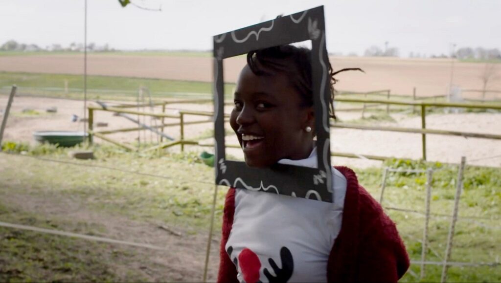 Un film dramatique | Éric Baudelaire Éric Baudelaire's Un film dramatique scene. Woman with a frame around her head smiles outdoors. Dramatic film still.