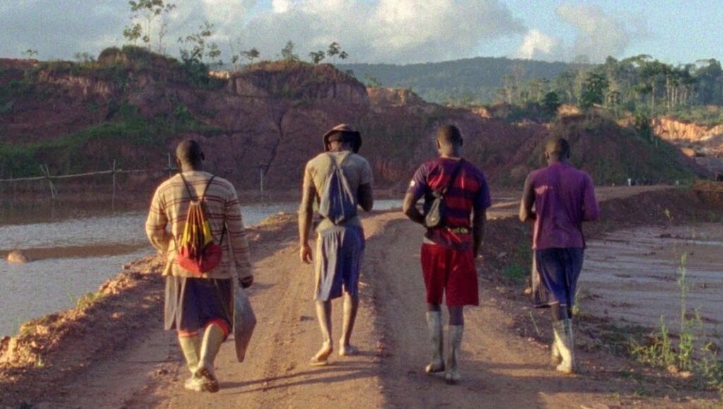 Good Luck film scene. Four men walk away on a dirt road toward a mining landscape.