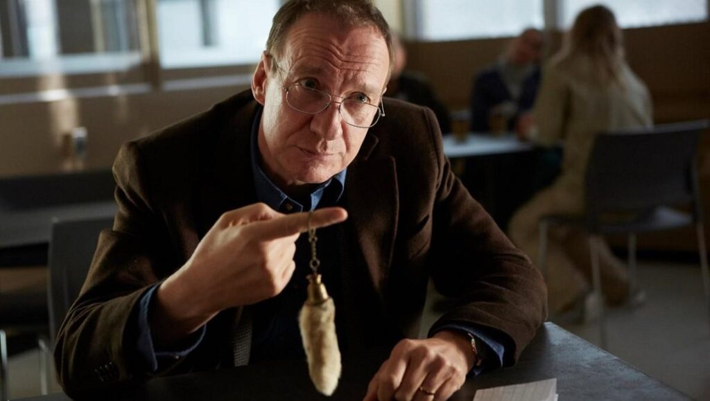 Actor in Guest of Honour movie. Man with glasses points to a rabbit's foot keychain. Atom Egoyan film.