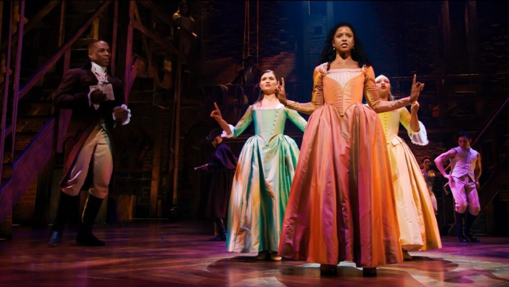Hamilton musical stage performance. Cast members in period costumes singing and acting.