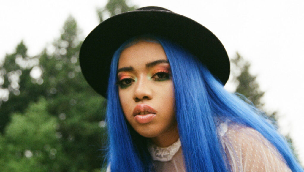 Jean Deaux, Krash era. Singer with blue hair, black hat, and colorful makeup.