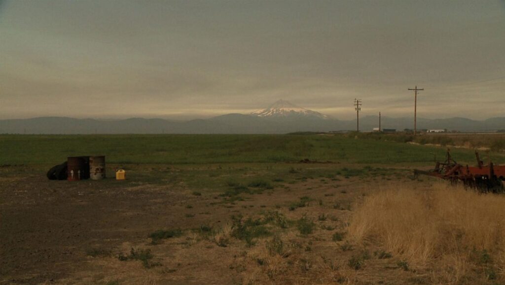James Benning's L. Cohen: Landscape with mountain, field, and rural objects. Moody, overcast sky.