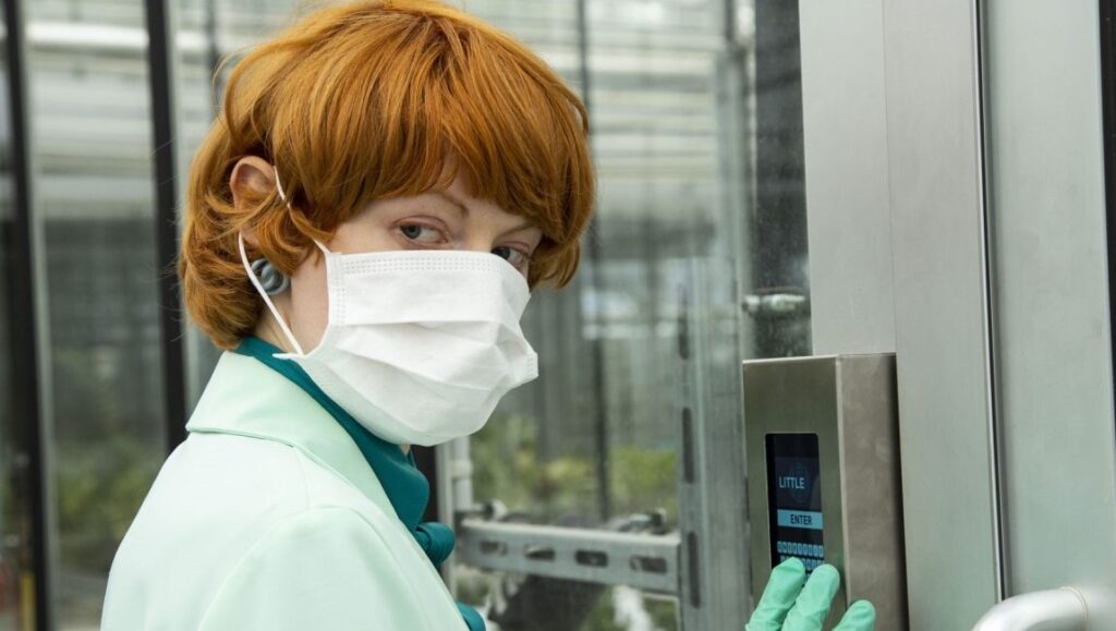 Still from Little Joe film. Woman in lab coat and mask enters passcode.