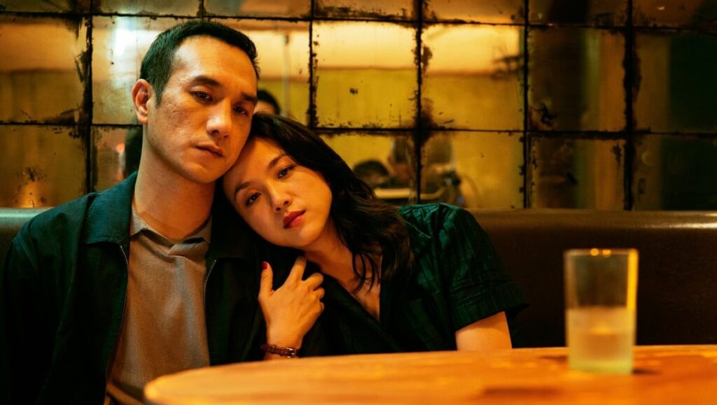 Long Day’s Journey Into Night | Bi Gan Long Day's Journey Into Night film still. Man and woman in dimly lit scene, glass of water. Bi Gan movie.