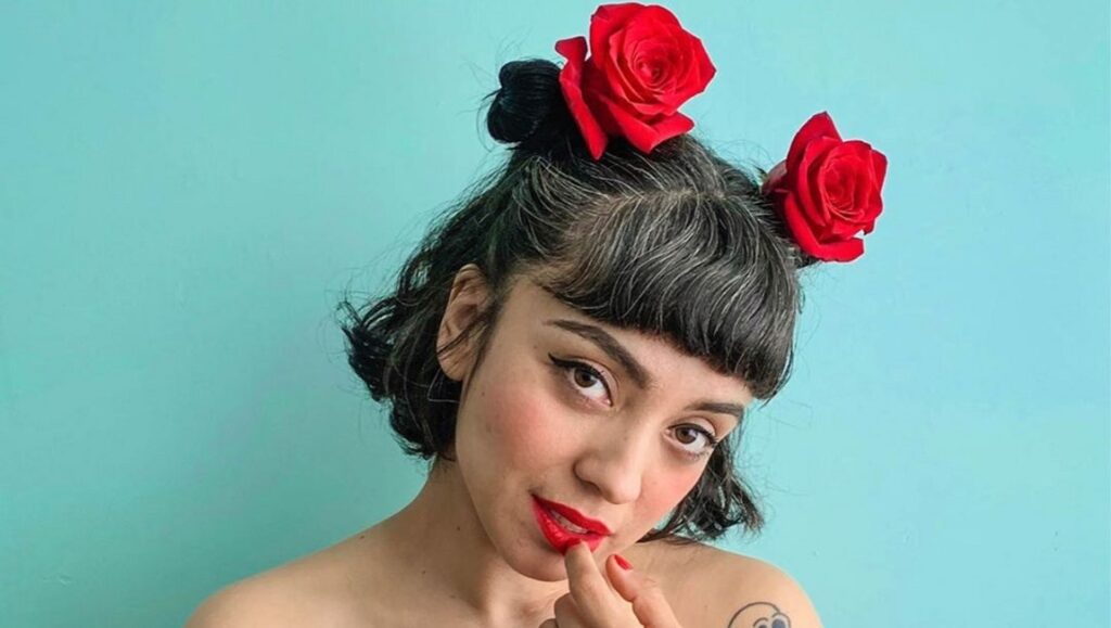 Mon Laferte | Norma Mon Laferte portrait. Norma album era. Singer with red roses in hair, red lipstick, and a tattoo.