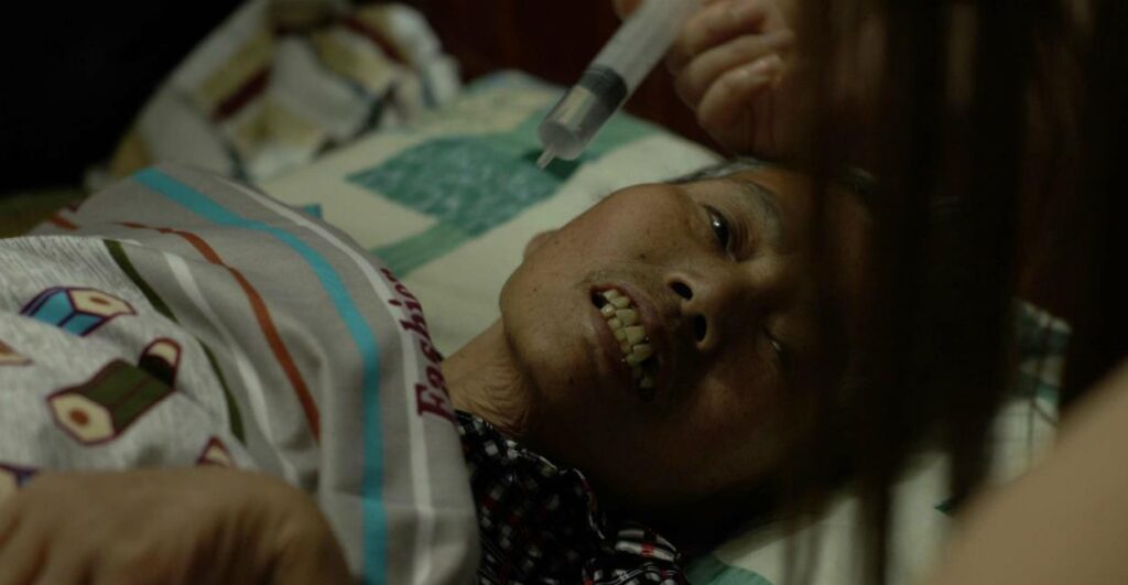 Mrs. Fang documentary film. An elderly woman lies in bed being fed with a syringe. Wang Bing film.