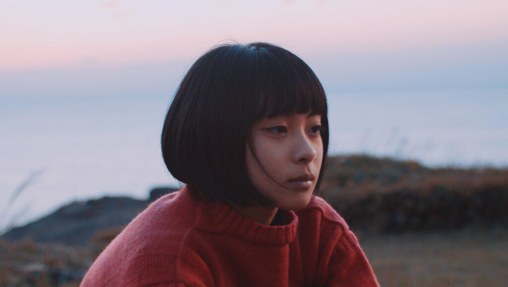 Our House | Yui Kiyohara Yui Kiyohara's Our House film still. Young woman with bob haircut, wearing red sweater, gazes pensively at dusk landscape.