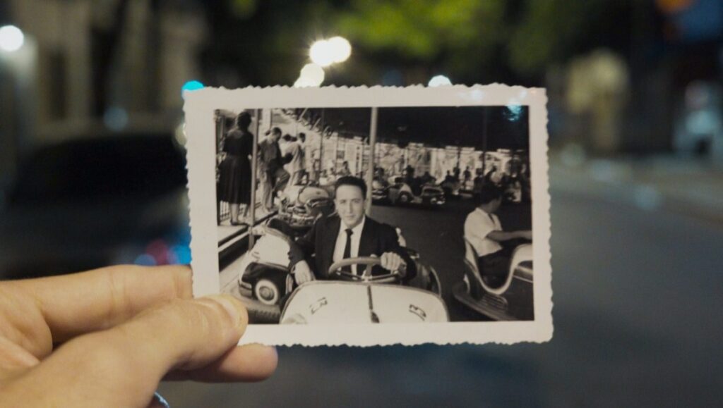 Private Fiction | Andres Di Tella Hand holding vintage photo. Man in bumper car. Andres Di Tella's Private Fiction film still. Black and white.