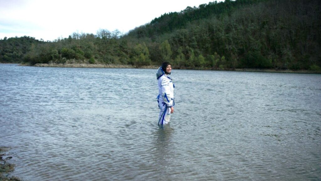 Alice Winocour's Proxima movie still: Astronaut in spacesuit stands in a lake, forest background.