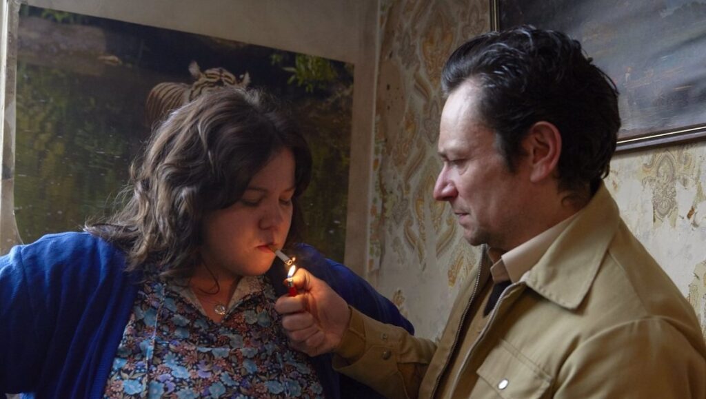 Ray & Liz still. Richard Billingham film scene: man lights woman's cigarette. Domestic, gritty realism.