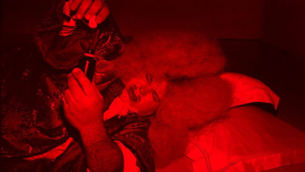Roi Soleil film still. Albert Serra's film in red lighting. Person holding a phone.