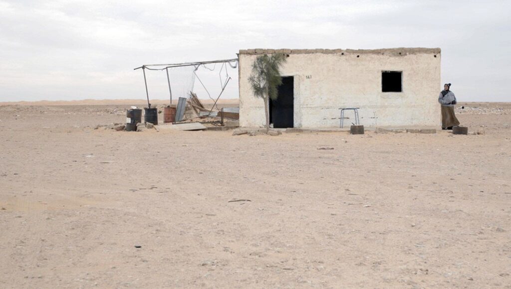 143 Sahara Street | Hassen Ferhani 143 Sahara Street: Desert landscape with a small building and a person standing outside. Arid, remote location.