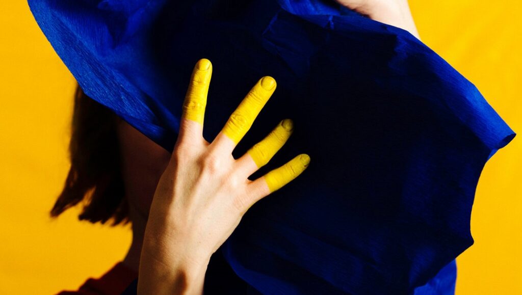Stine Janvin | Fake Synthetic Music Stine Janvin's Fake Synthetic Music art. Yellow painted fingers holding blue fabric against a yellow background.