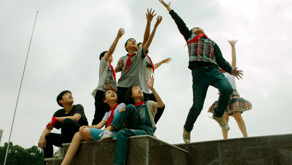 Suburban Birds | Qiu Sheng Suburban Birds film scene: Group of young actors reaching up, wearing red scarves.