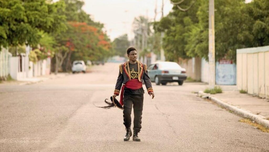 The Day Shall Come | Christopher Morris The Day Shall Come movie still. Marching man in costume with hat on street. Christopher Morris film.