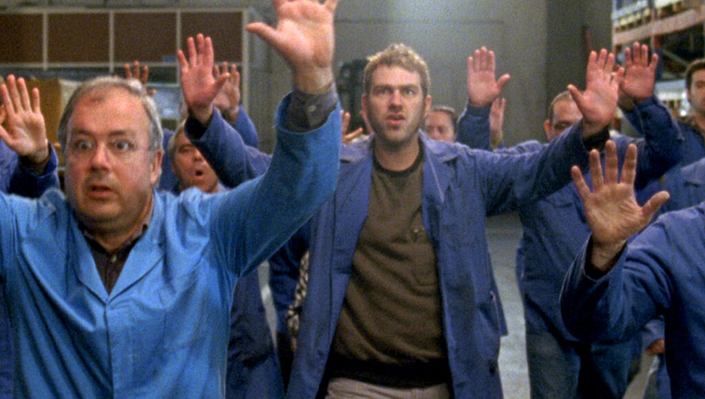 The Nothing Factory | Pedro Pinho The Nothing Factory film still. Factory workers in blue uniforms raise their hands in unison. Pedro Pinho film.