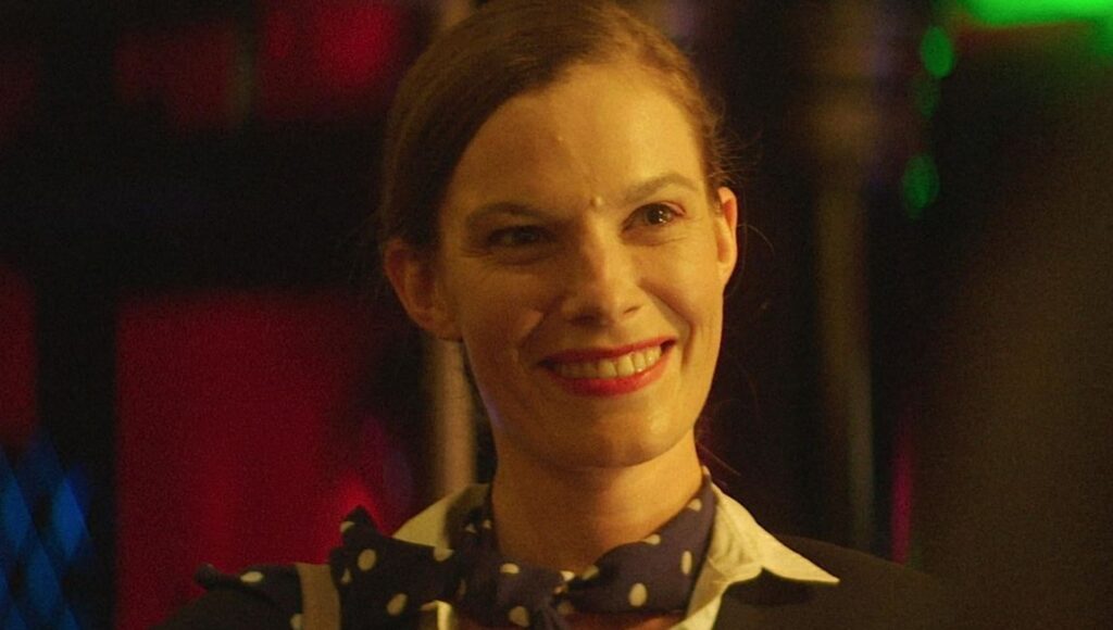 Thirst Street film still: Woman smiles with red lipstick, polka dot scarf. Nathan Silver movie.