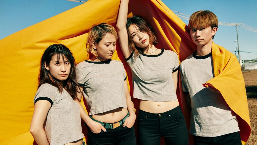 Tricot | Repeat Japanese rock band Tricot. Four members in t-shirts with yellow backdrop.