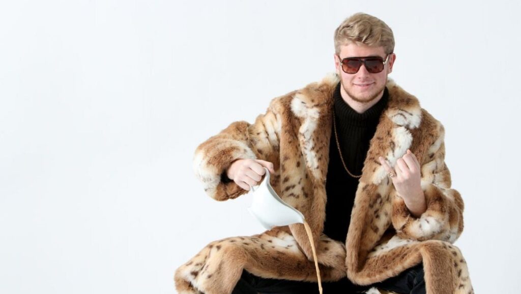 Yung Gravy, sensational rapper, wearing a fur coat and sunglasses. He is pouring a drink.
