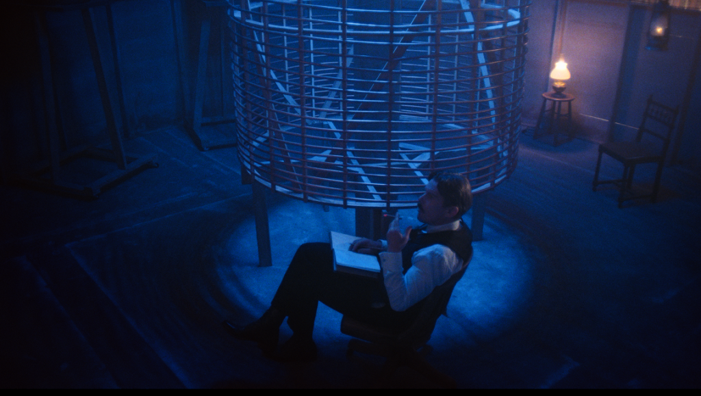 Tesla | Michael Almereyda Nikola Tesla in Michael Almereyda's film 'Tesla'. Man sits with notebook under a large Tesla coil.