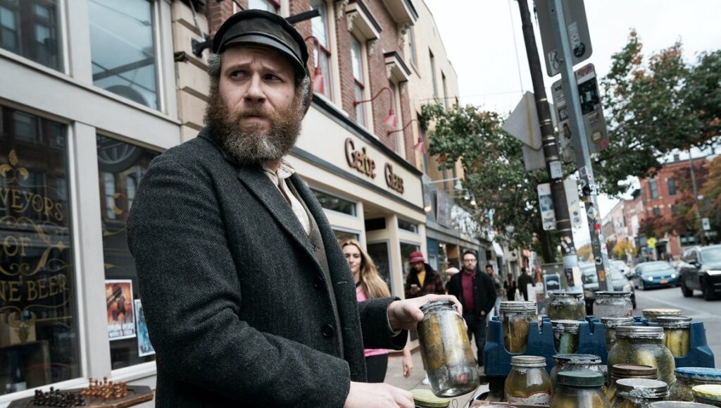 Seth Rogen in An American Pickle movie. Bearded man selling pickles from a cart on a city street.