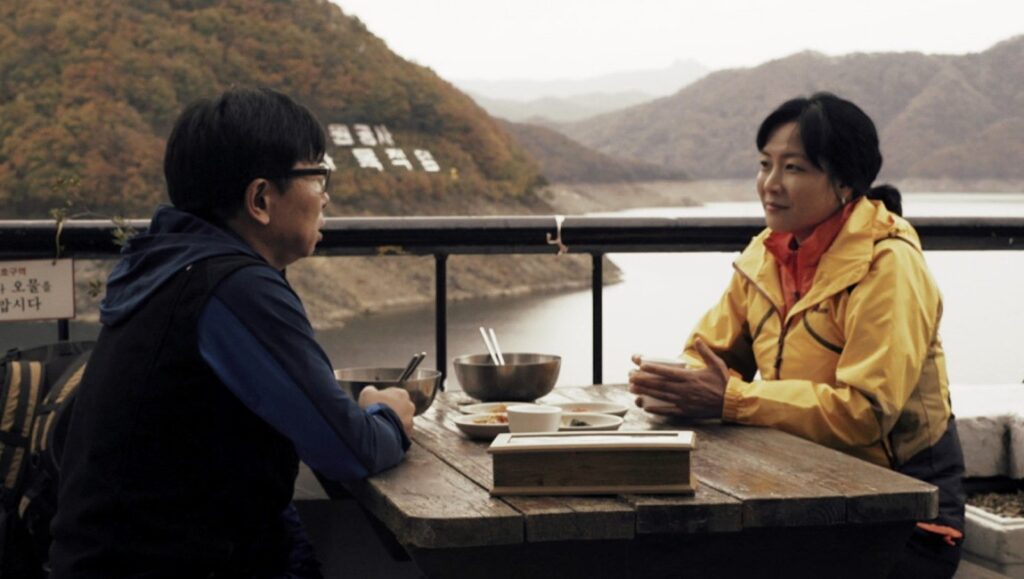 Autumn, Autumn | Jang Woo-jin Autumn, Autumn by Jang Woo-jin. Two people eating outdoors with a lake and mountains in the background.