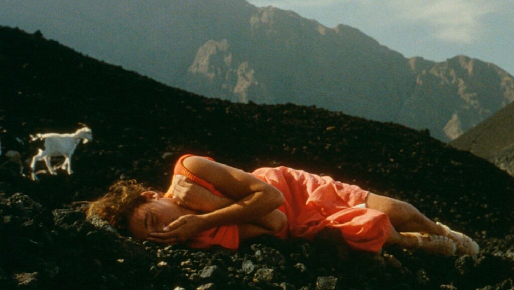 Casa de Lava film still. Woman in red dress lies on volcanic rock with goats, mountains in background. Pedro Costa film.