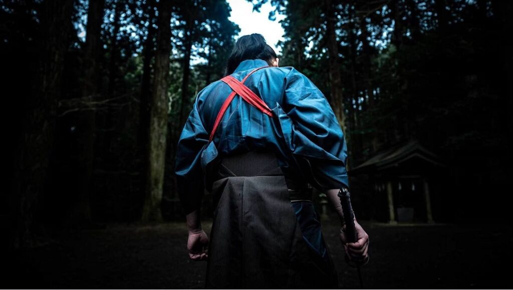 Crazy Samurai: 400 vs. 1 | Yuji Shimomura Fantasia Fest: Back view of a samurai in traditional garb, standing in a dark forest, holding a sword.