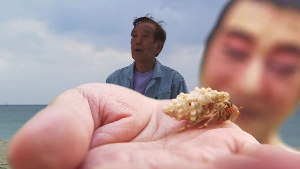 Hengyoro film still. Man holding a hermit crab, Gō Takamine film.