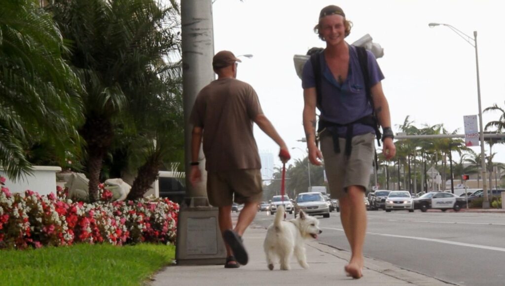 I Am Another You: Nanfu Wang film still. Two men and a small white dog walk on a city sidewalk.
