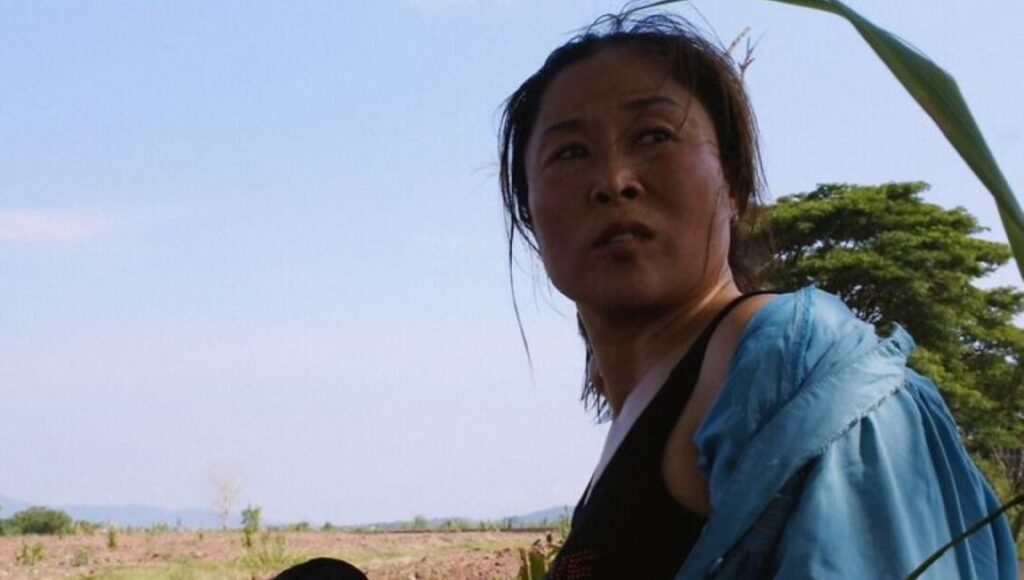 Mrs. B, a North Korean Woman | Jero Yun Mrs. B, a North Korean woman, looks off-camera. Jero Yun film still of a woman in a field.