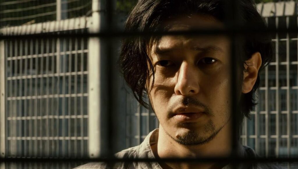 Over the Fence movie still. Actor Joe Odagiri behind a fence, directed by Nobuhiro Yamashita.