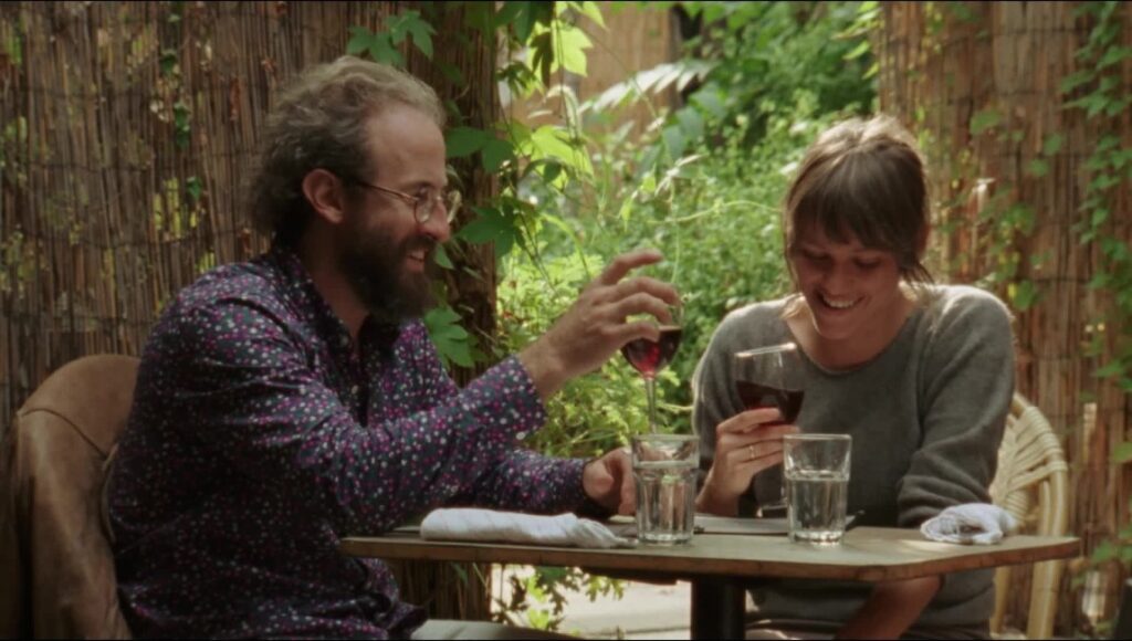 Person to Person movie scene: Man and woman at a table, drinking wine and smiling.