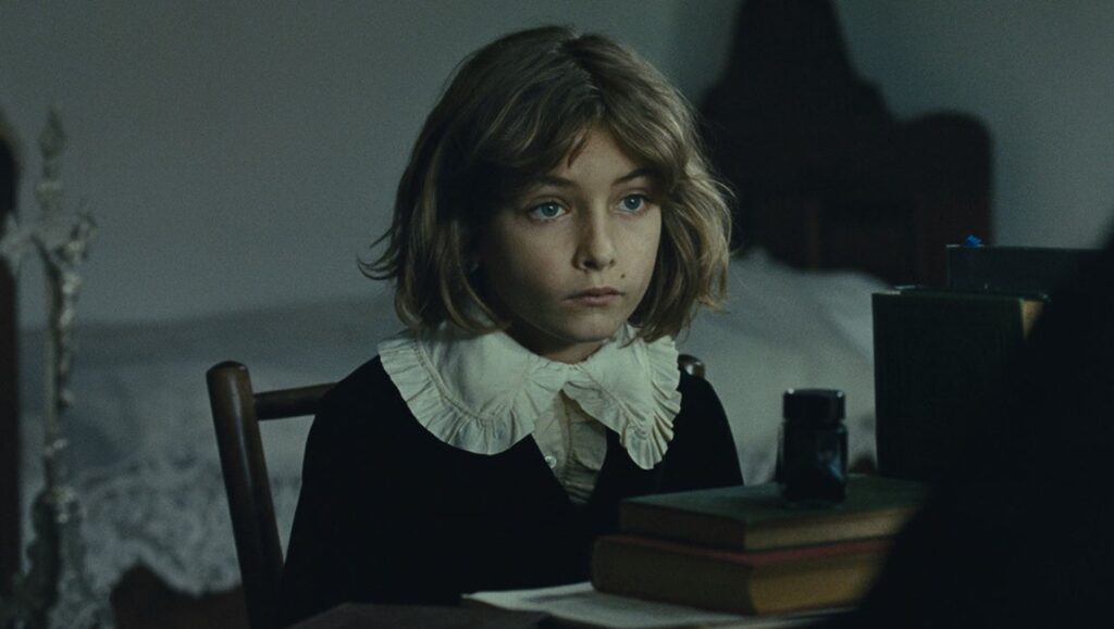 The Childhood of a Leader film still. Young boy with ruffled collar sitting at a desk.