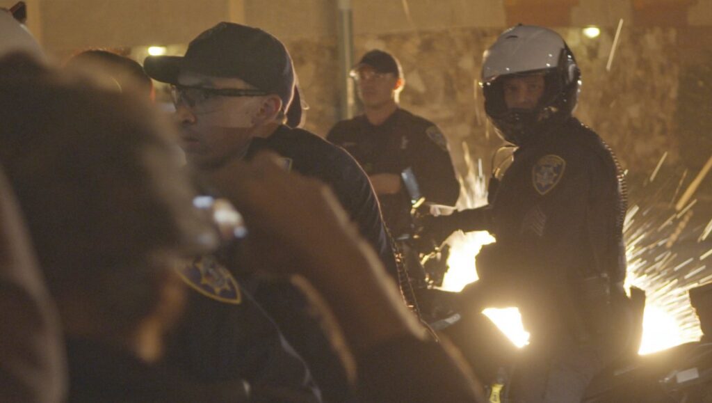 Scene from The Force documentary. Police officers in riot gear amid sparks and activity.
