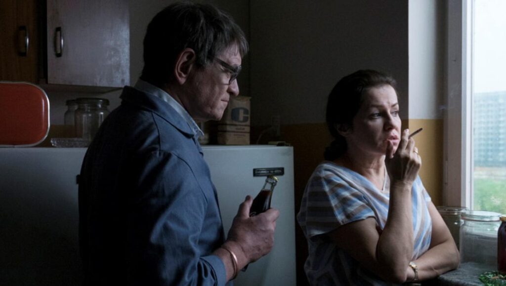 Still from The Last Family film. Man opens a soda, woman smokes by the window. Jan P. Matuszyński movie.