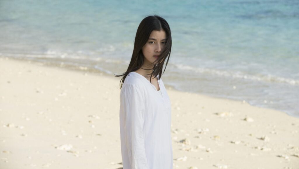 The Shell Collector | Yoshifumi Tsubota Yoshifumi Tsubota's The Shell Collector: Woman in white on a sandy beach with turquoise water.