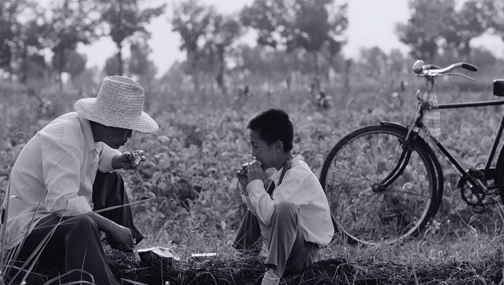 The Summer Is Gone film still. Black and white image of a man, boy, and bicycle in a field.