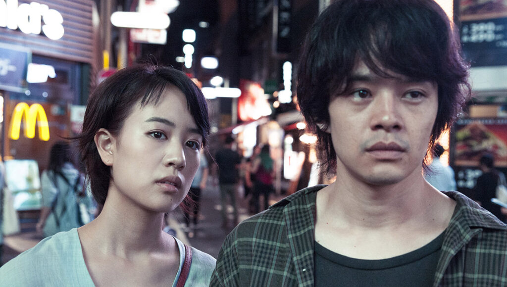 The Tokyo Night Sky film scene: Asian couple in Tokyo. Night lights, McDonald's in background. Yûya Ishii movie.