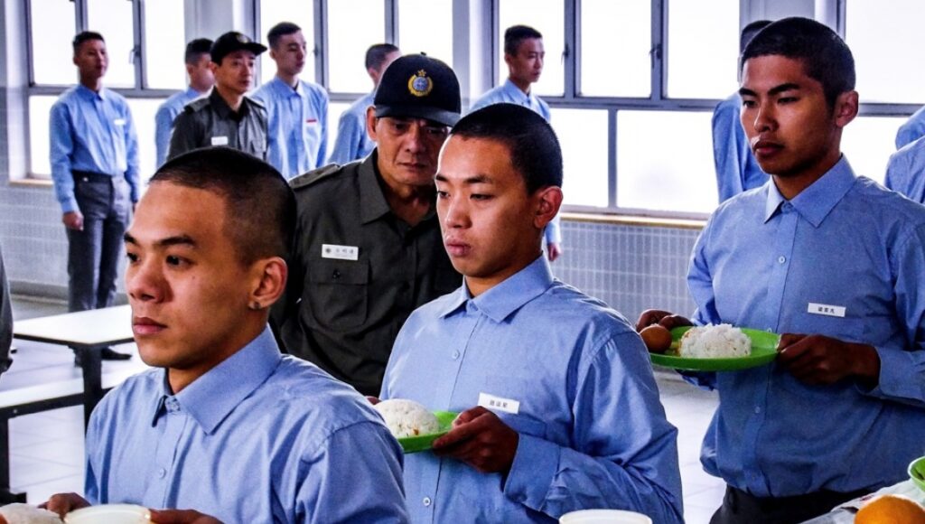 Andrew Wong Kwok-Kuen With Prisoners scene. Prisoners in blue uniforms holding food trays, guarded by an officer.