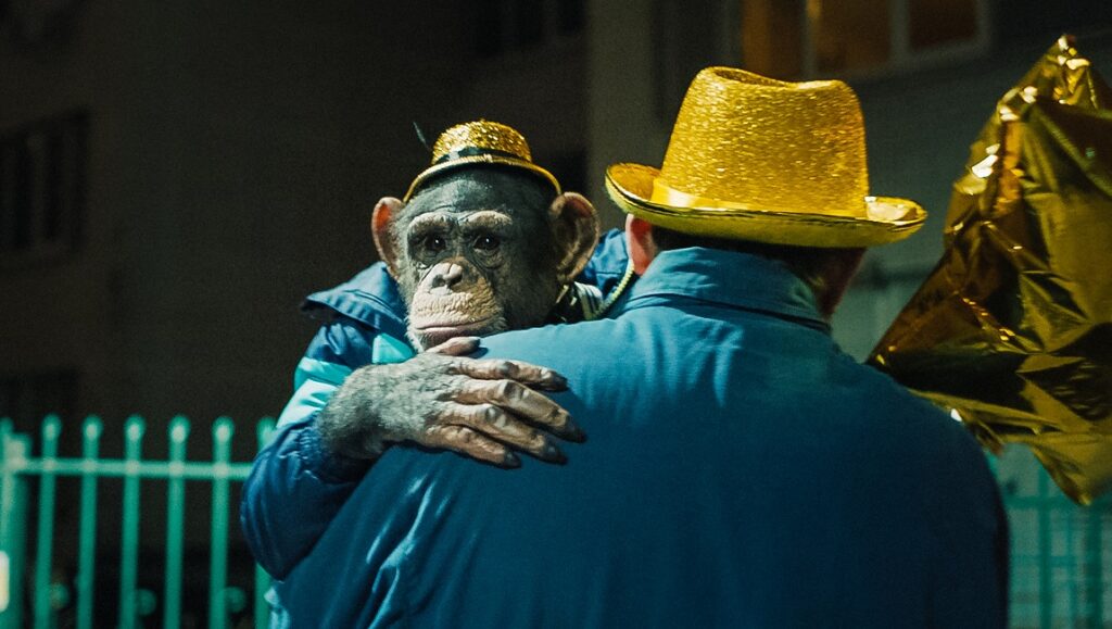 Space Dogs film still: Chimpanzee in a hat embraces a man. Golden hats and foil visible.