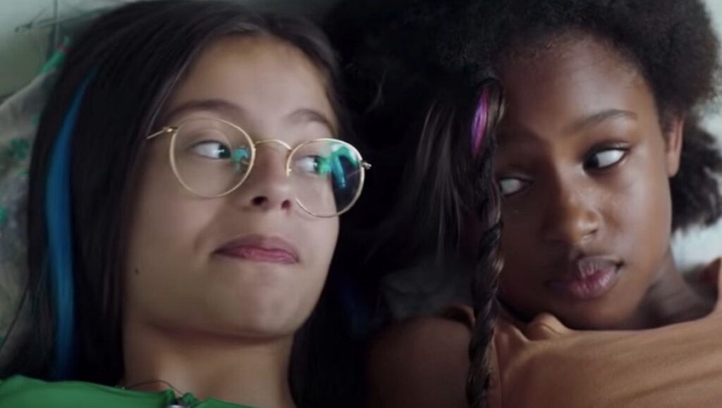 Two girls from Cuties movie, one with glasses and blue hair, the other with purple hair, looking sideways.