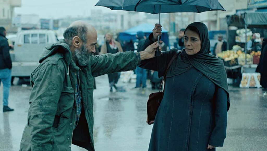 Gaza Mon Amour film still: Man and woman with umbrella in a rainy market. Arab cinema.
