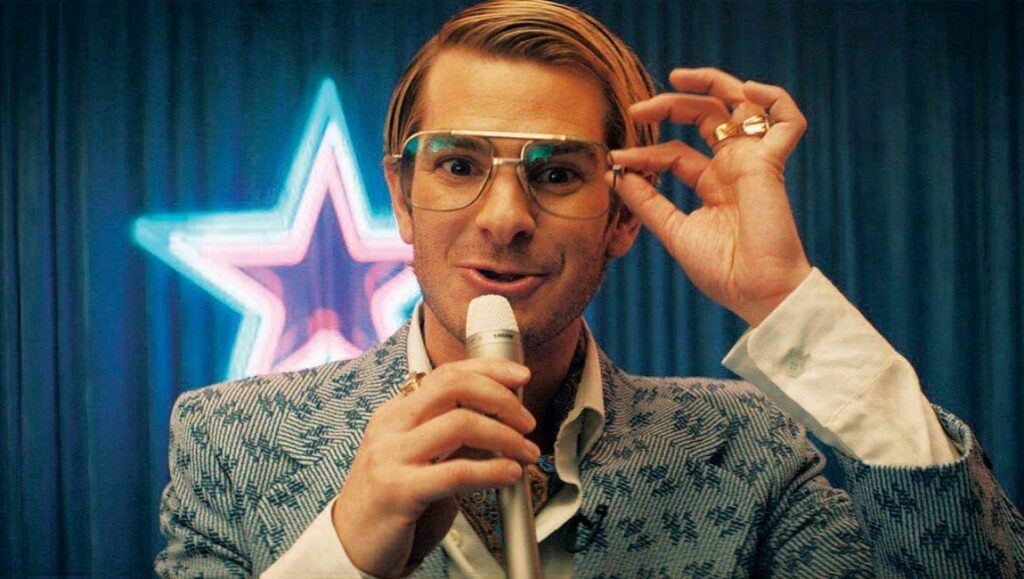 Venice International Film Festival 2020 — Dispatch 1: Mainstream, City Hall, Notturno Andrew Garfield at Venice Film Festival 2020 for Mainstream. Man with mic, glasses, and star backdrop.
