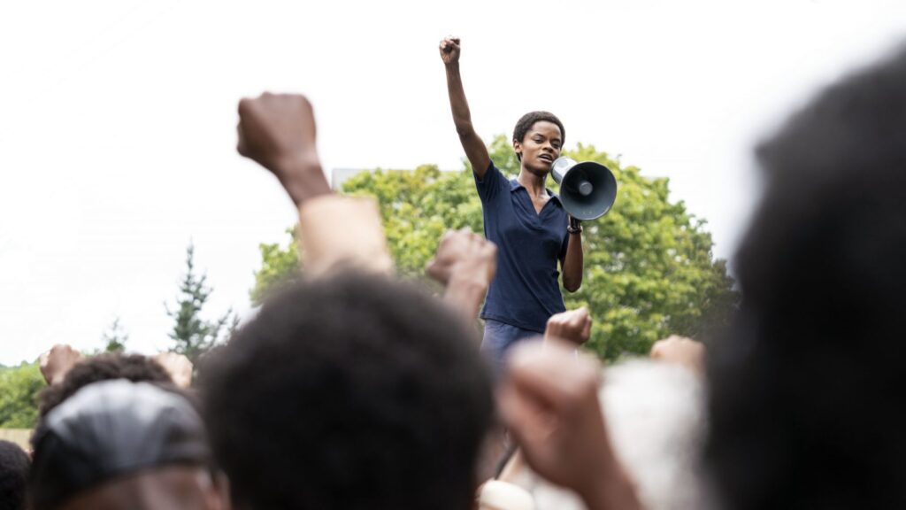 Mangrove film still: Letitia Wright rallies crowd with a megaphone, fists raised in protest. NYFF 2020.