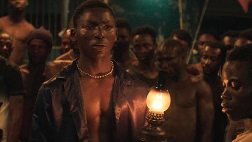 Venice International Film Festival 2020 — Dispatch 3: Night of the Kings, Saint-Narcisse, The Ties Still from Night of the Kings at Venice Film Festival. Man holding lamp surrounded by other men.