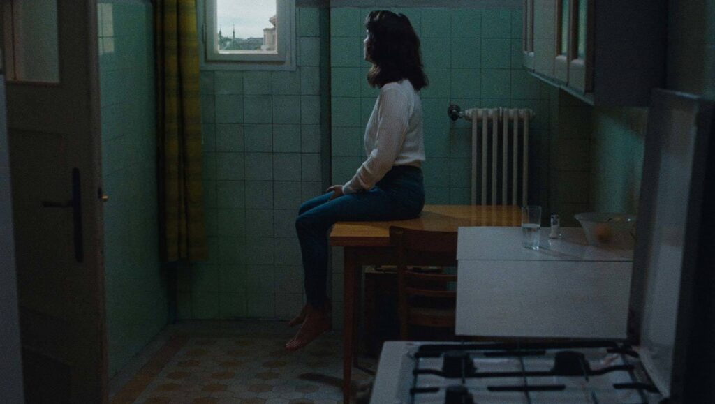Preparations to Be Together for an Unknown Period of Time | Lili Horvát Preparations to Be Together for an Unknown Period of Time film still. Woman sits on table in kitchen. Lili Horvát movie.